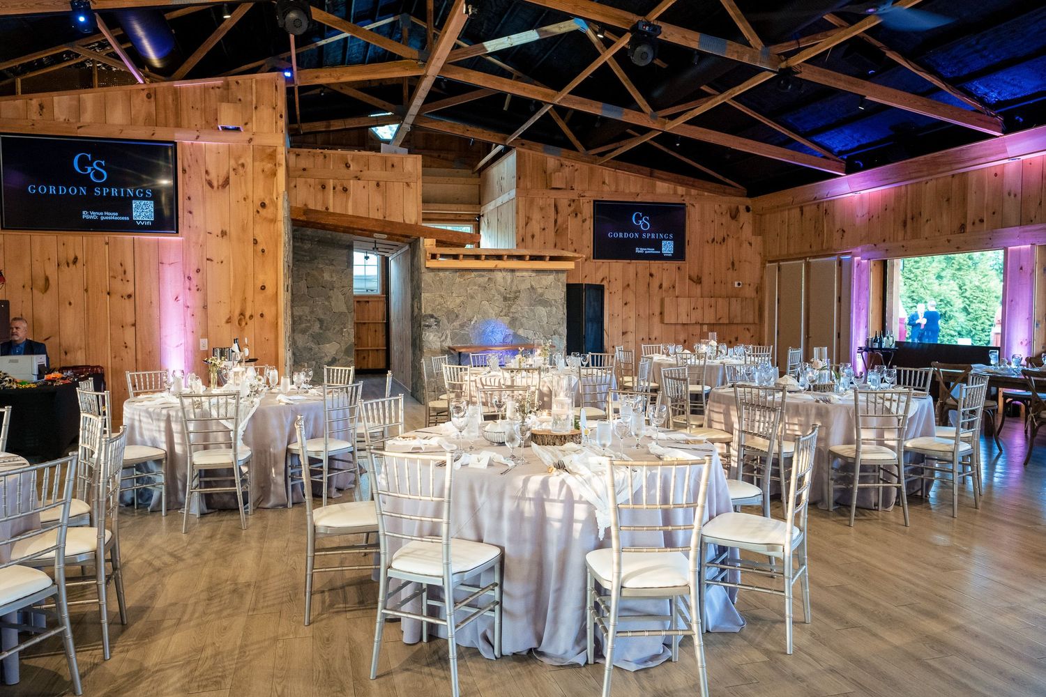 Elegant wedding reception hall with round tables, chiavari chairs, and warm rustic wood walls.
