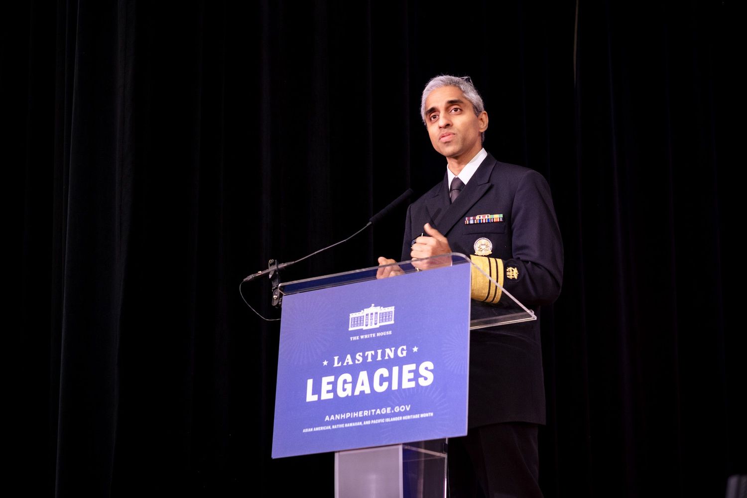 US Surgeon General speaks at a Lasting Legacies podium on a dark stage.