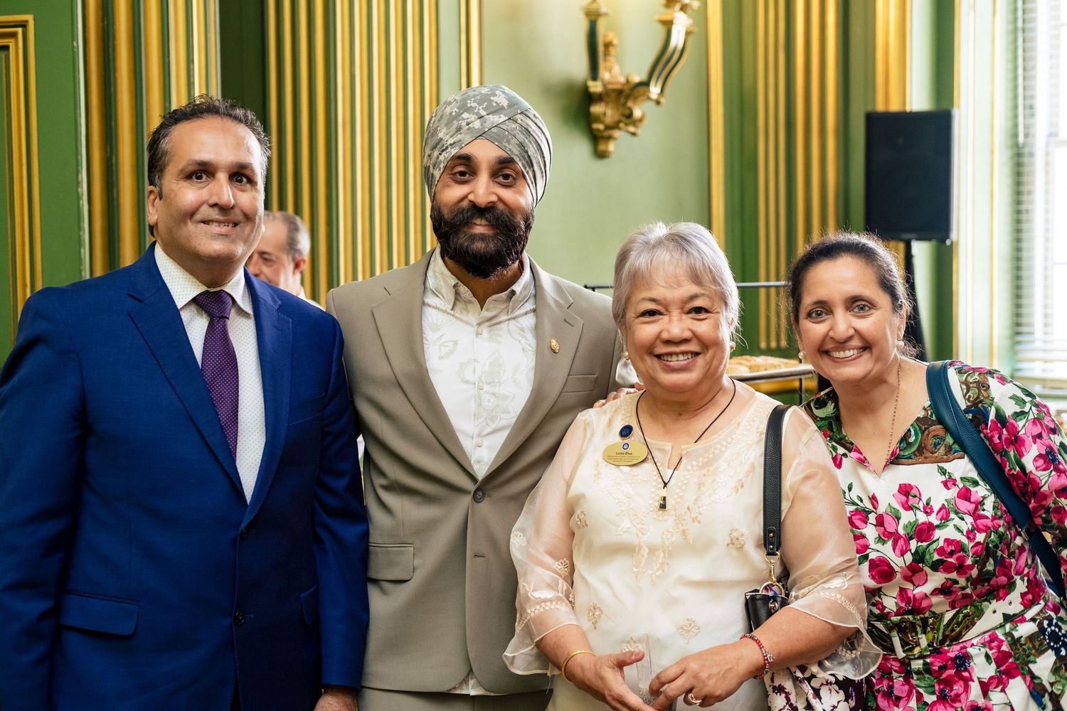 Four people smiling together in an elegant green-walled room at a formal gathering or reception event.