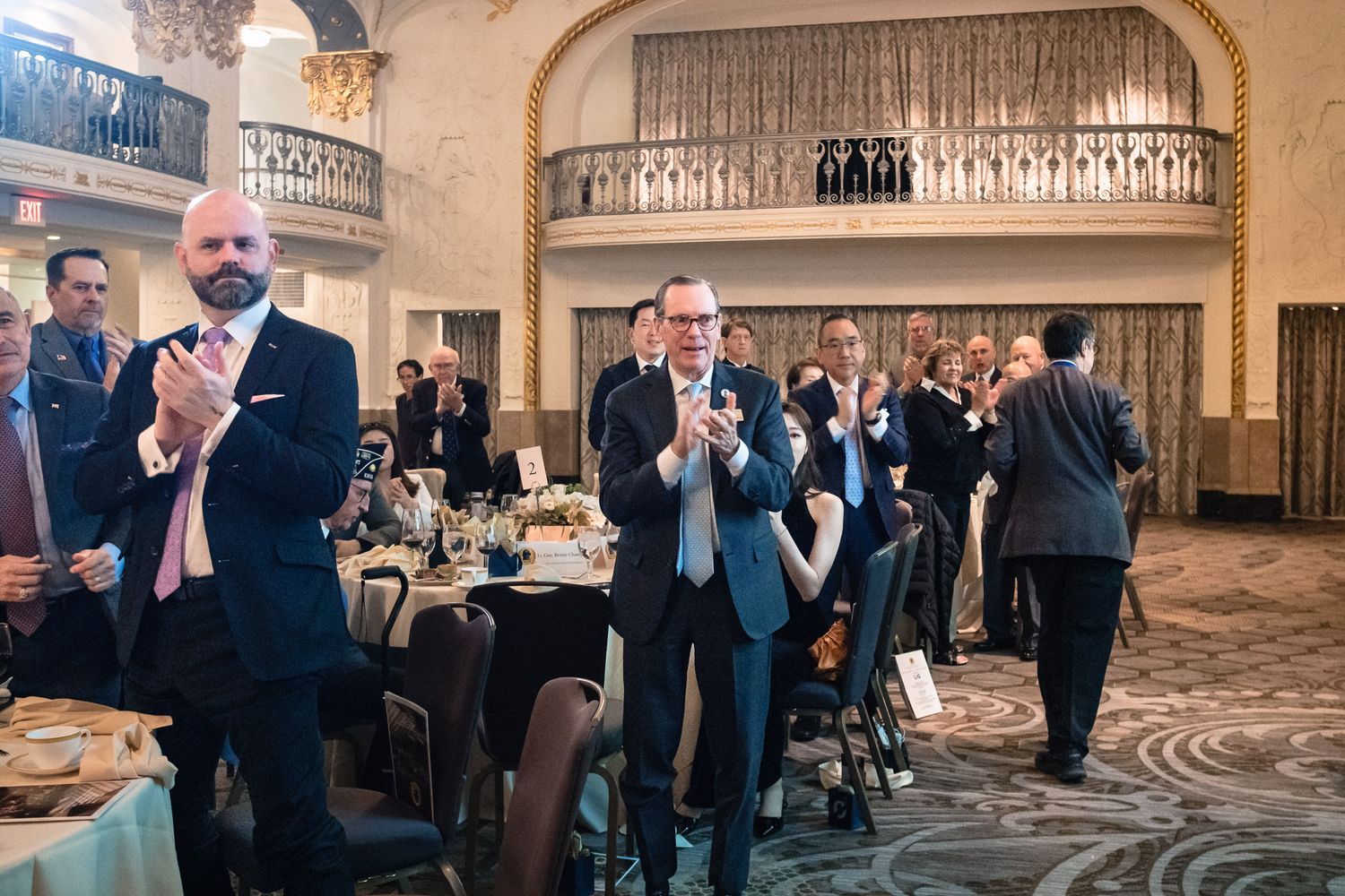 Guests applaud in elegant ballroom during formal dinner event at ornate venue.
