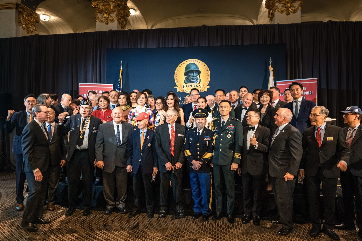 Military officers and veterans pose for a group photo at a formal ceremony with a blue backdrop.