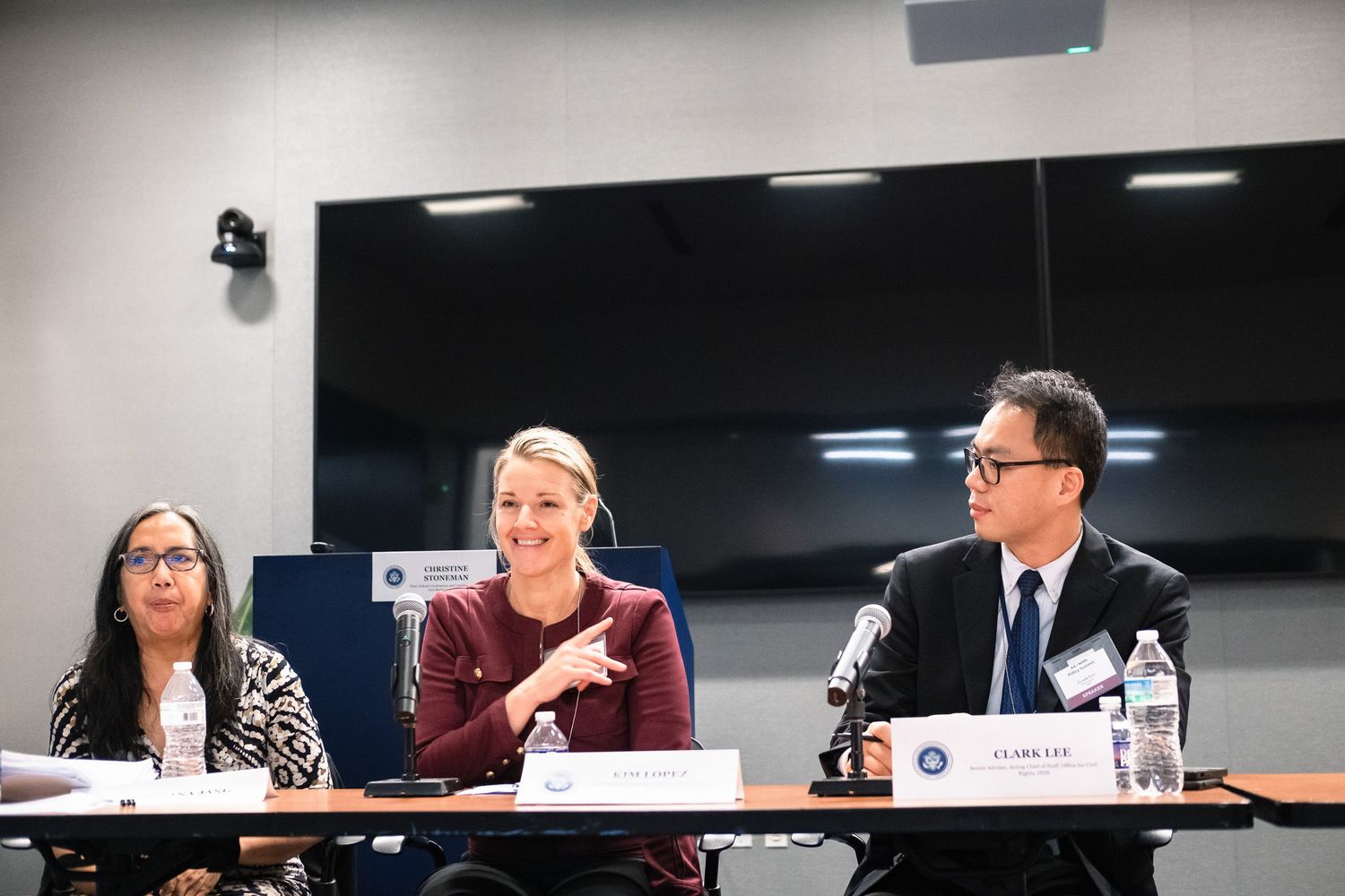 Three panelists seated at a conference table with microphones, engaged in discussion at a professional panel event.