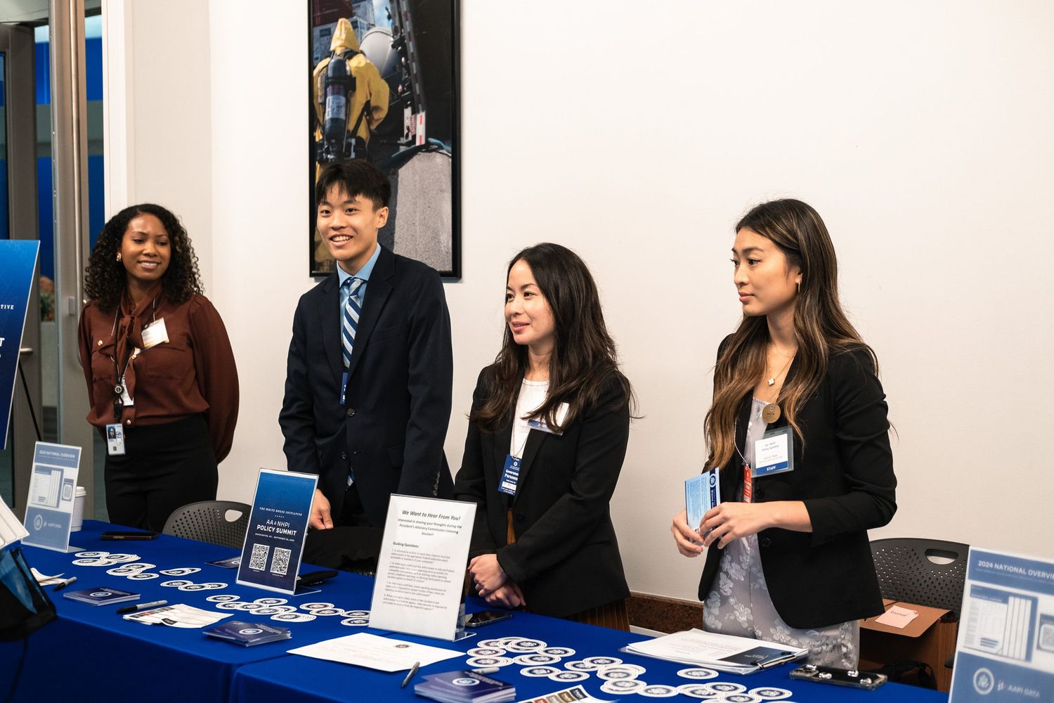 Four professionals stand at a blue-draped exhibit table at a career fair, smiling and ready to engage visitors.
