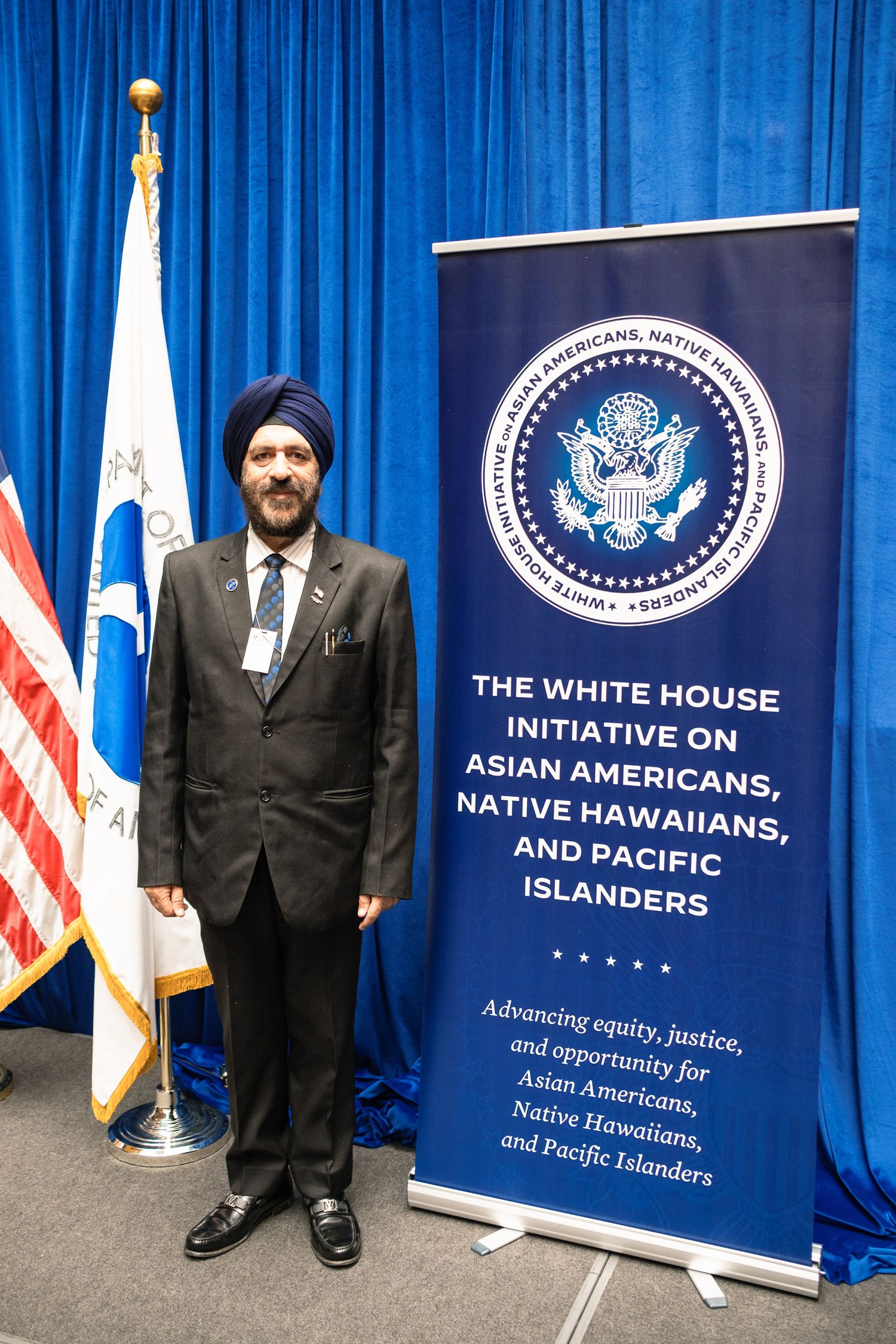 Man in blue turban and suit stands beside White House Initiative on Asian Americans, Native Hawaiians, and Pacific Islanders banner.