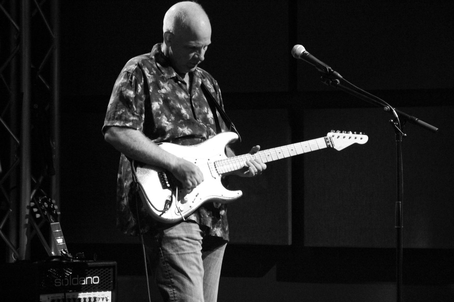 Musician playing electric guitar on stage in black and white concert photo with microphone stand.