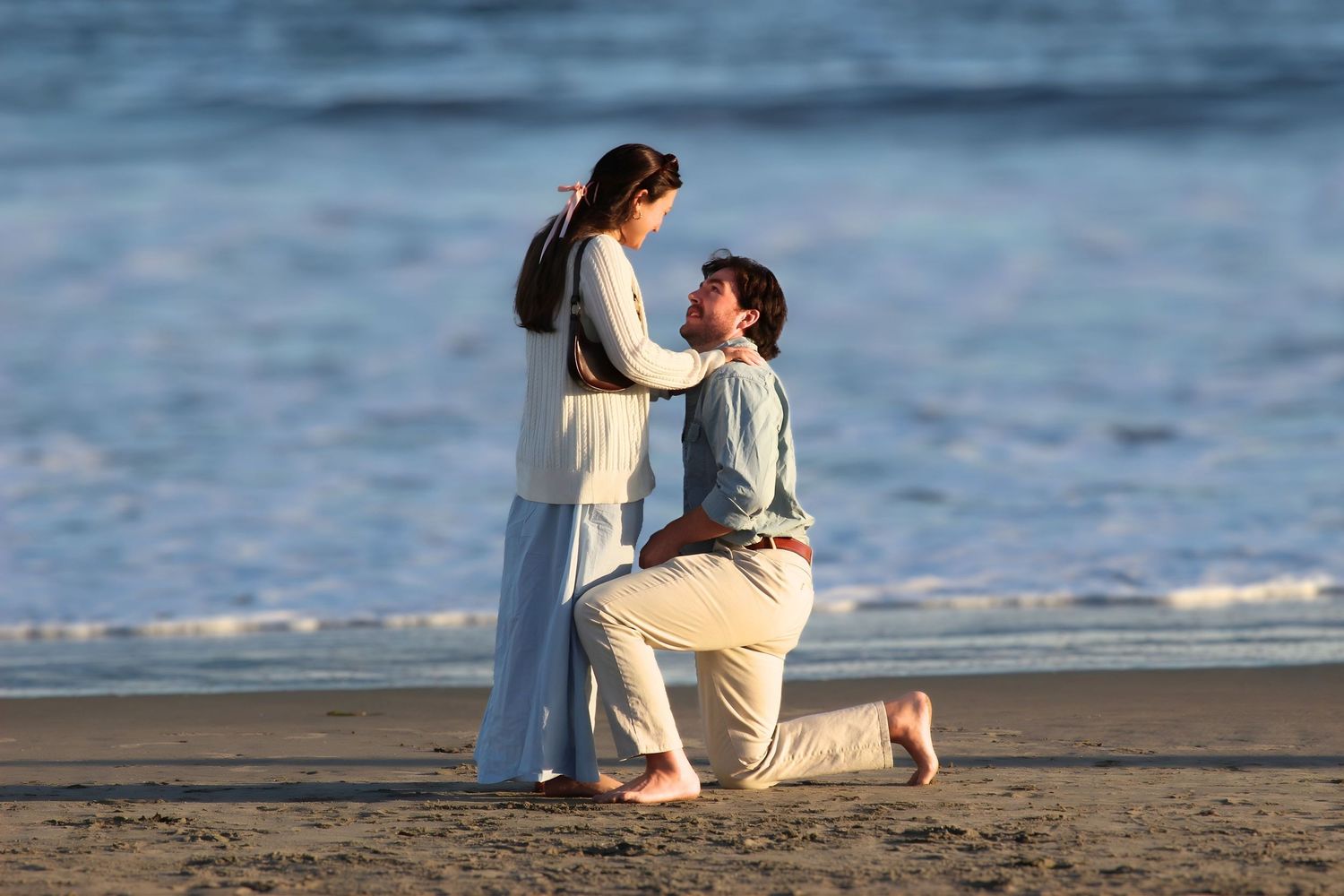 Man proposing to woman on a sandy beach at sunset in a romantic seaside marriage proposal.