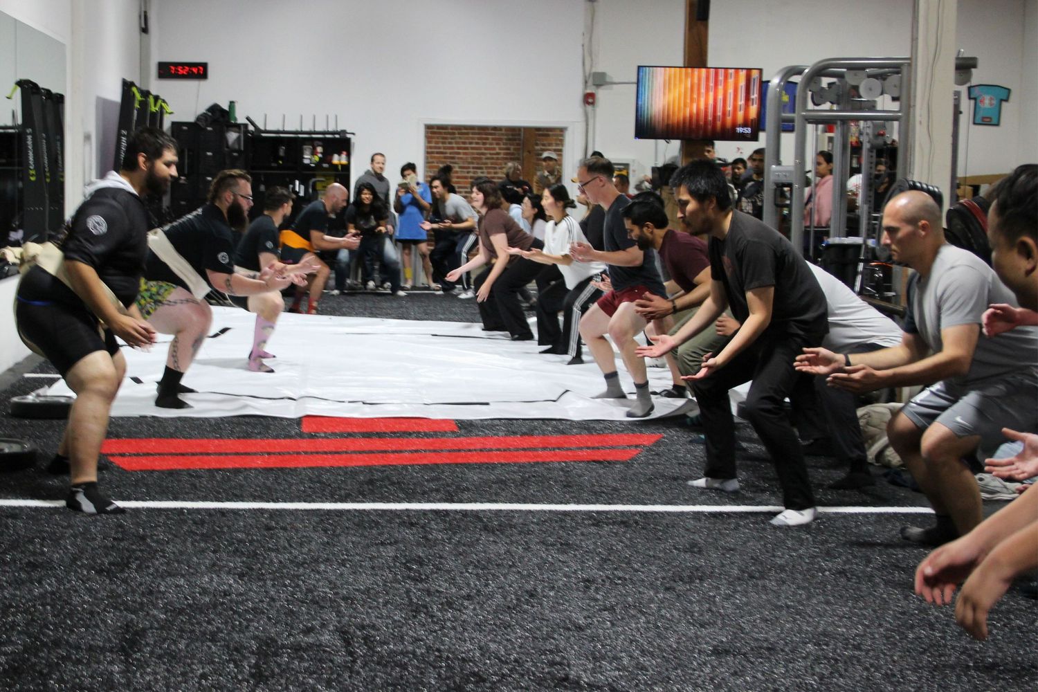 Group of people competing in a tug-of-war exercise at an indoor gym fitness event with spectators watching.