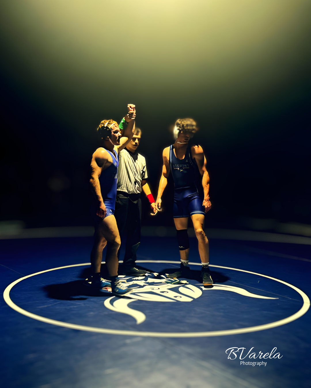 Wrestler's hand raised in victory under dramatic spotlight on a blue wrestling mat. sport photographer