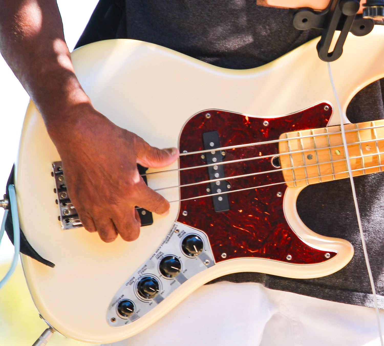 Close-up of a musician playing a white Fender bass guitar with red tortoiseshell pickguard on stage.