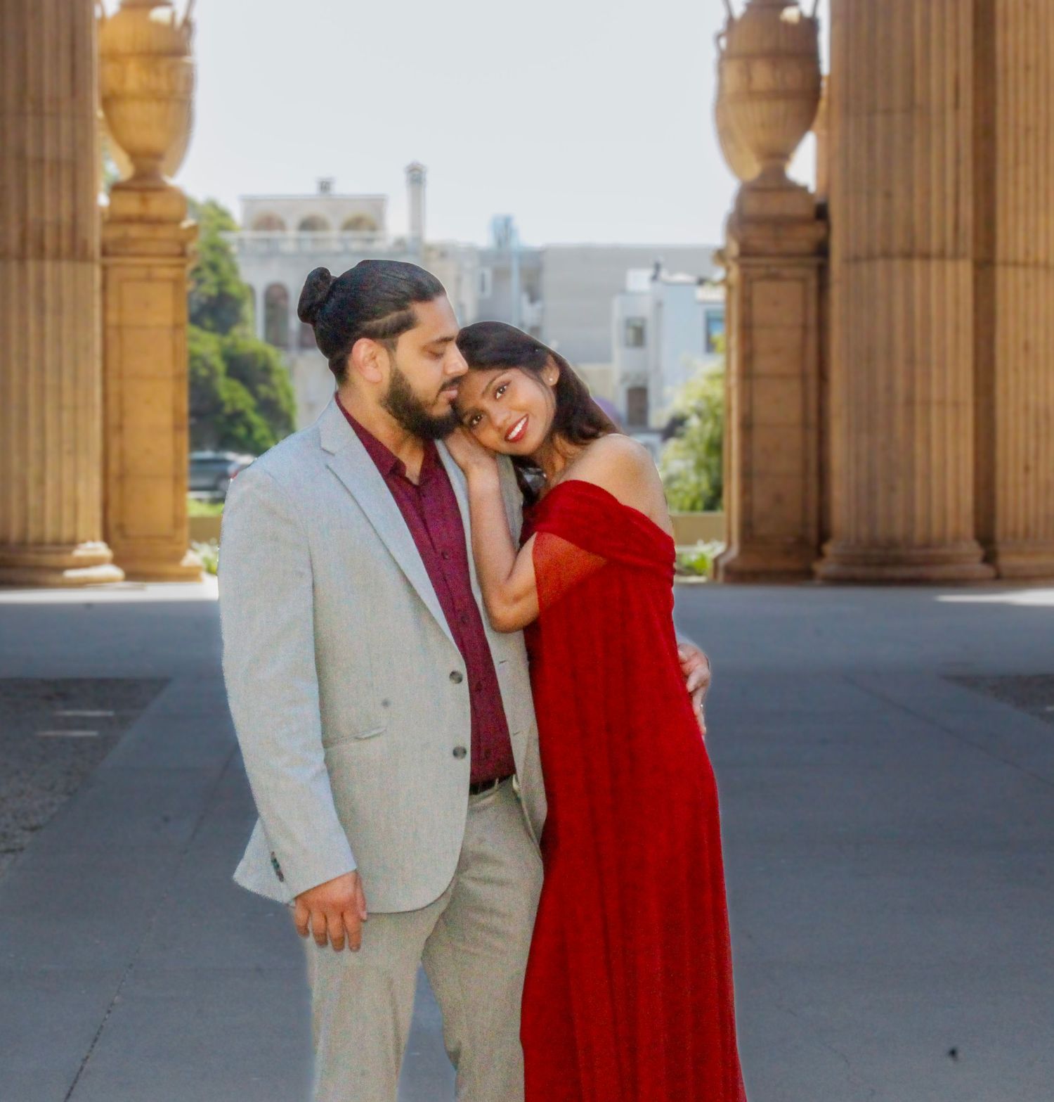 Couple posing at Palace of Fine Arts, woman in red gown leaning on man in gray suit, San Francisco.