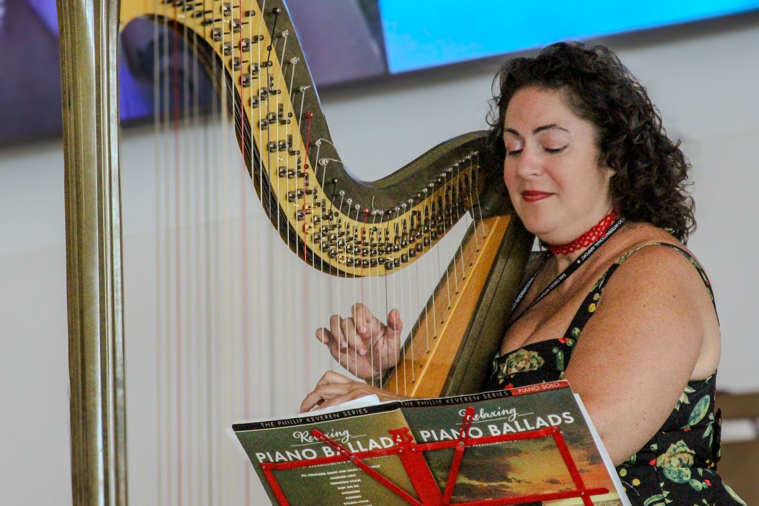 Woman with curly hair playing a golden harp, with Piano Ballads sheet music displayed in front of her.