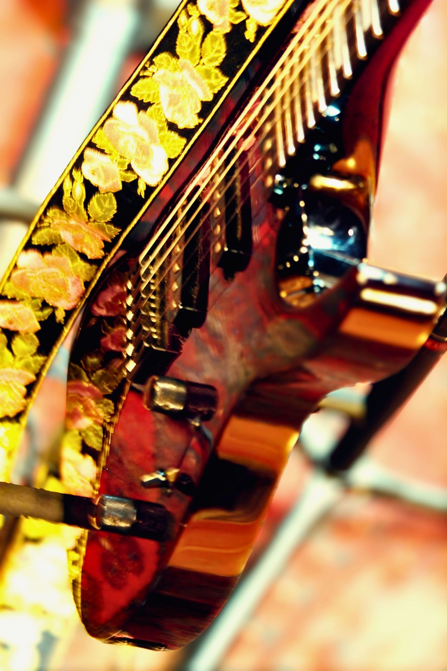 Close-up of an ornate guitar headstock with golden floral inlay design and tuning pegs against a brick background.