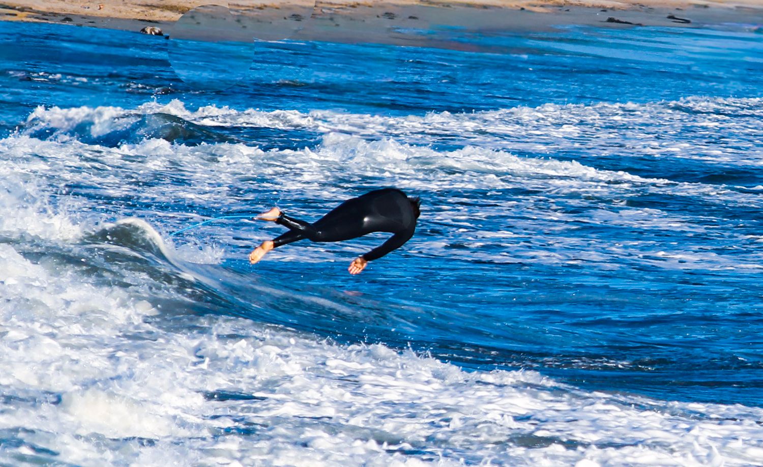 Surfer in black wetsuit riding a wave on a blue ocean, capturing an action-packed surfing moment.