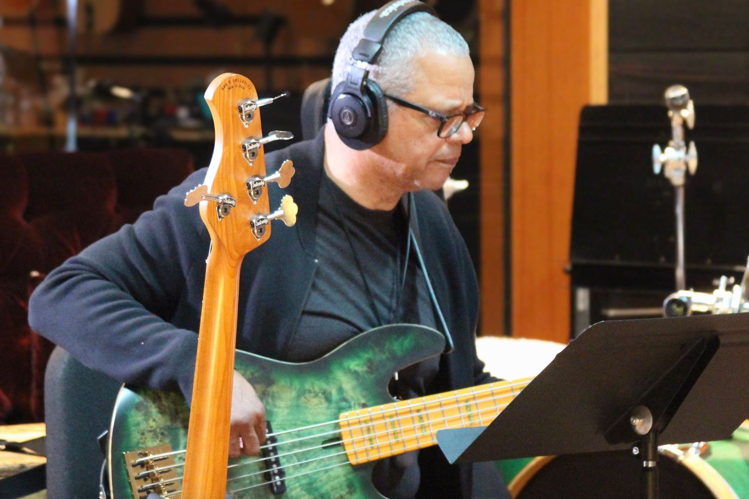 Musician playing a green bass guitar with headphones in a recording studio.