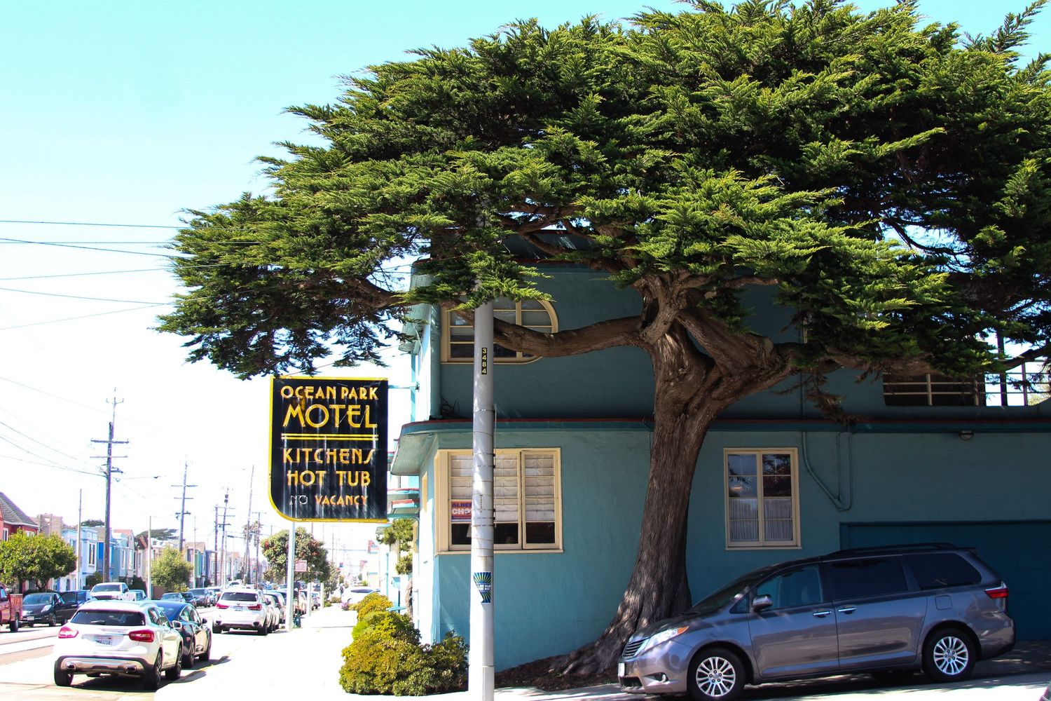 Ocean Park Motel sign with kitchen and hot tub amenities, beside a large cypress tree and teal building.