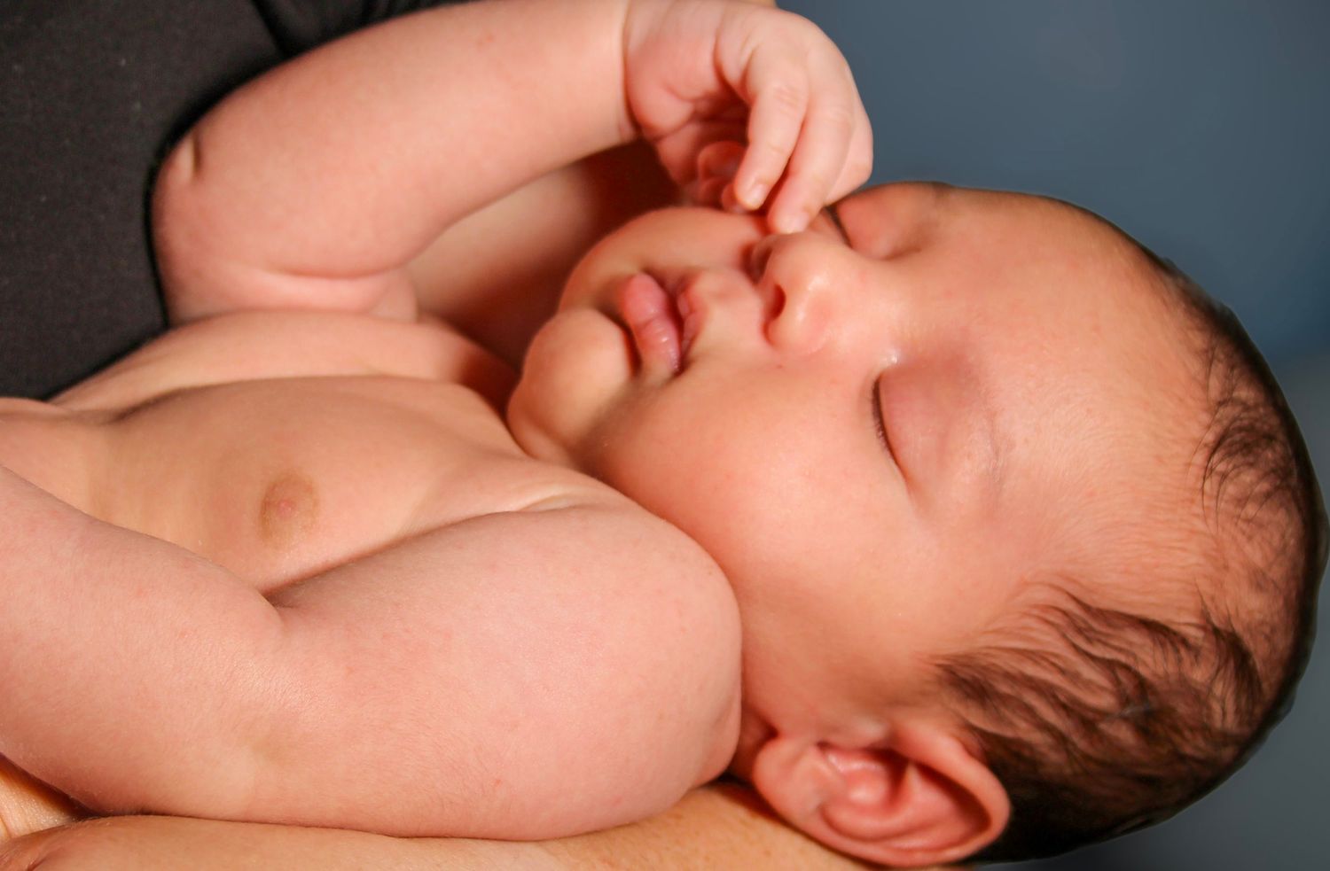 Peaceful newborn baby sleeping on parent's chest with tiny fist raised to face.