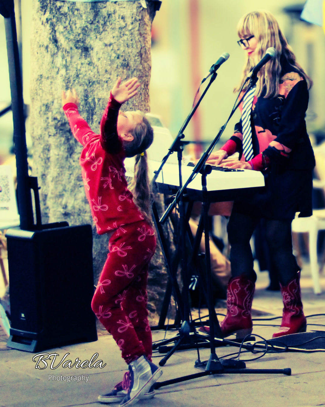 A young girl in red pajamas dances joyfully while a woman plays keyboard on an outdoor stage.
