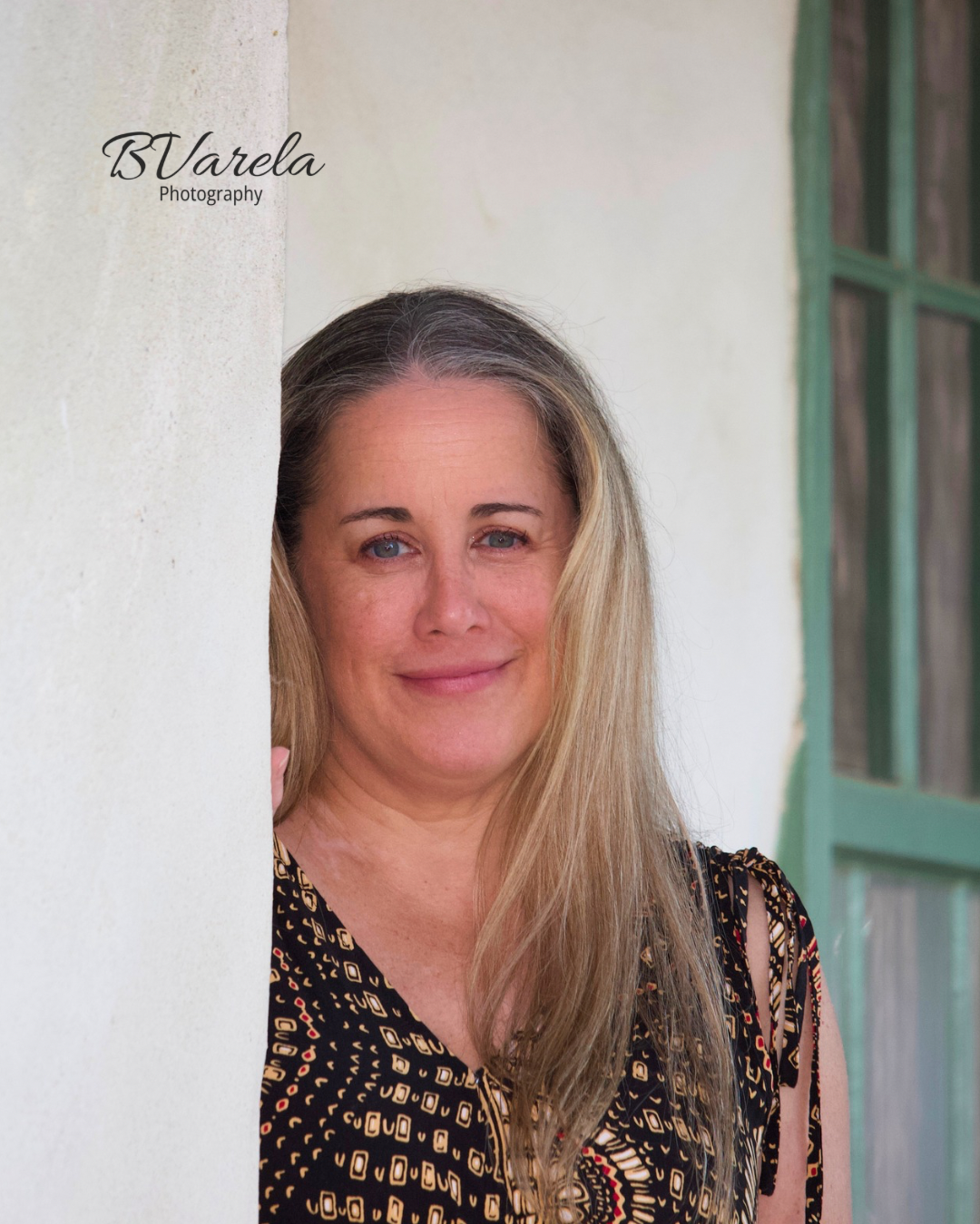 Woman with blonde hair leans against white wall near green door, photographed by BVarela Photography. tri-valley photographer