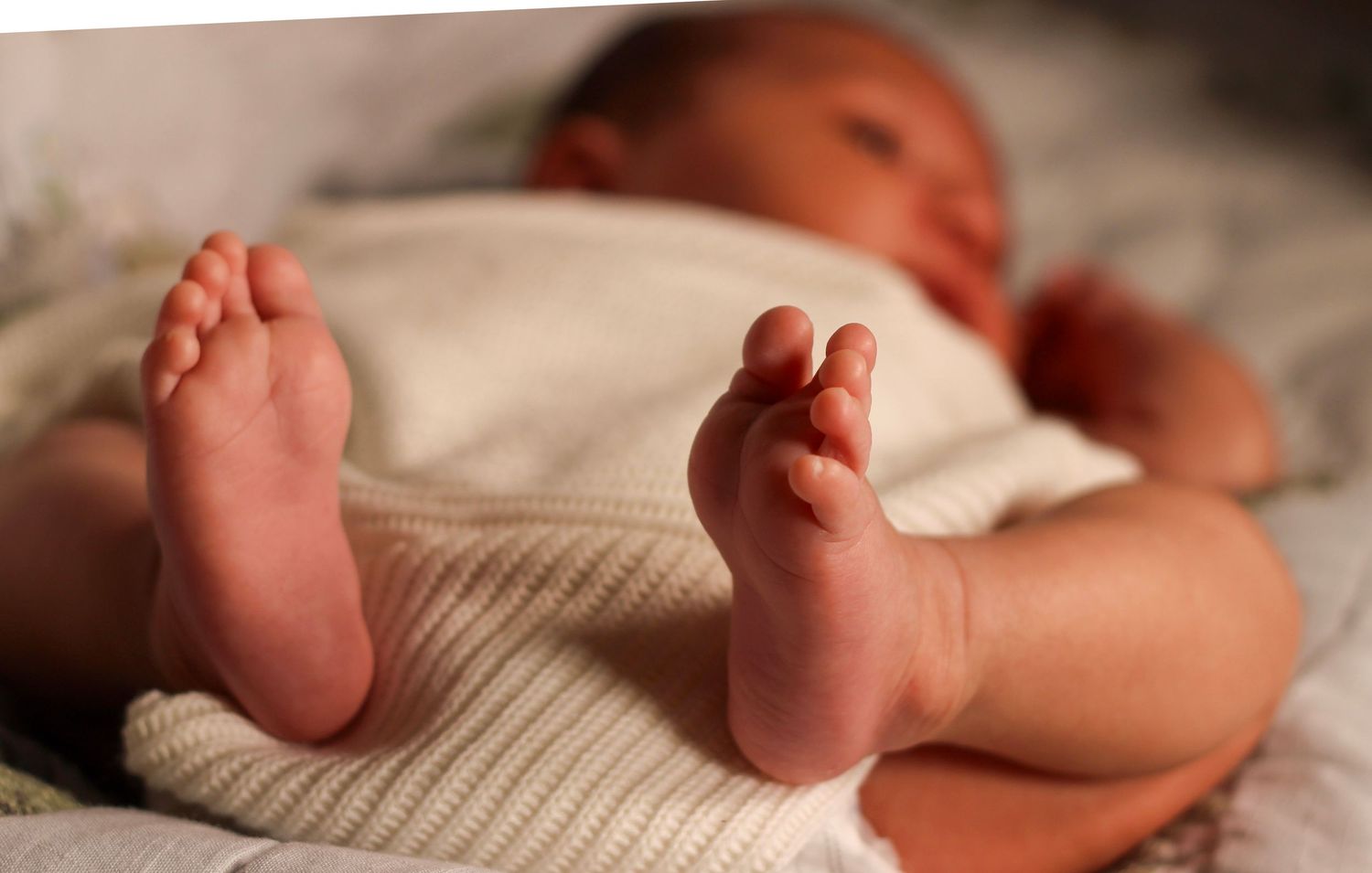 Close-up of a newborn baby's tiny feet and toes lying on a soft white blanket.