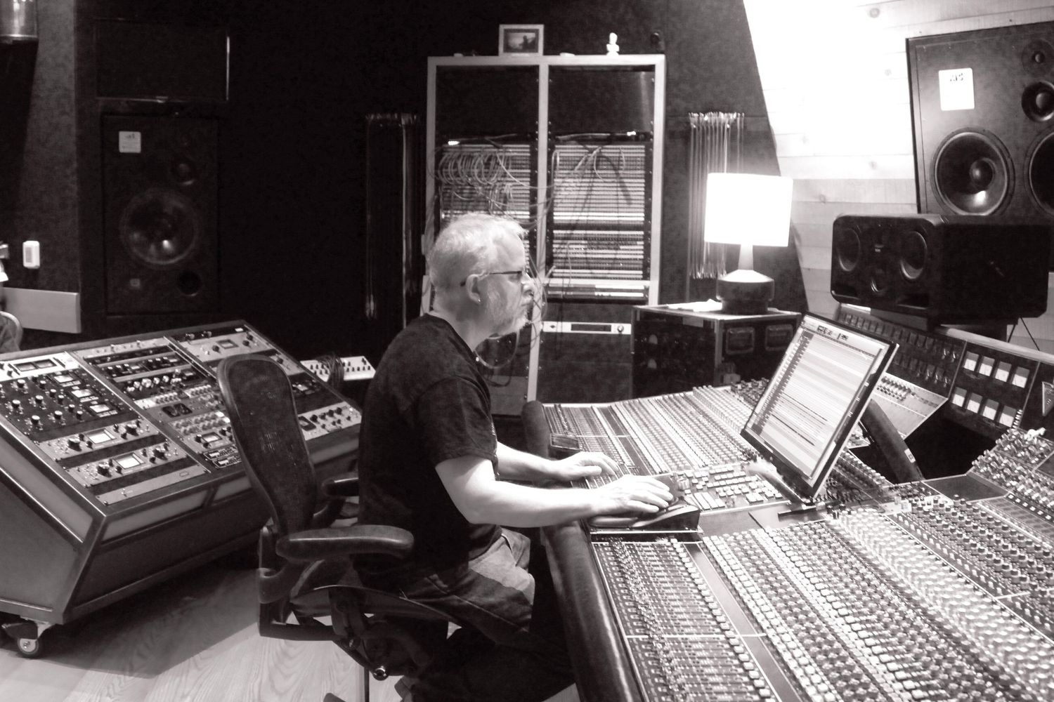 Music producer working at a professional recording studio mixing console with monitors and equipment.