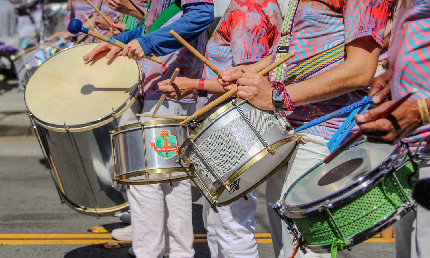 Colorful street performers playing snare drums during a vibrant outdoor festival parade.