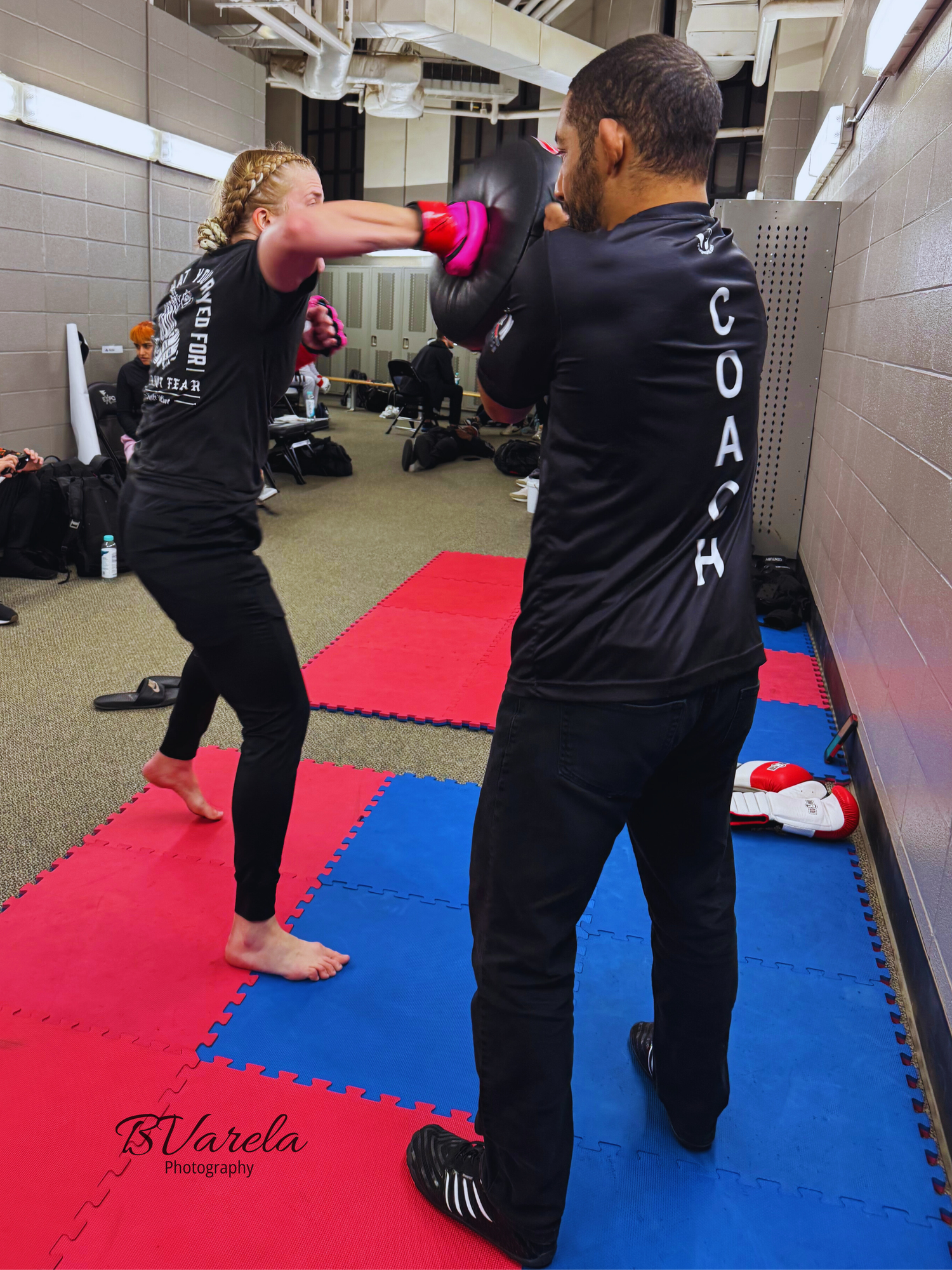 A coach holds a punch mitt while a female boxer practices striking during a kickboxing training session indoors.
