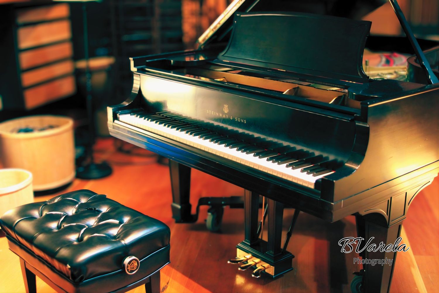 A shiny black grand piano with ivory keys beside a tufted leather bench in a warmly lit music studio.