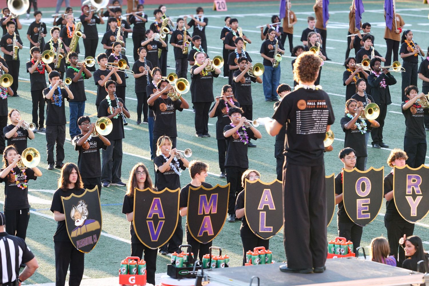 Avalon marching band performs on field in black uniforms, playing brass instruments with a conductor leading.