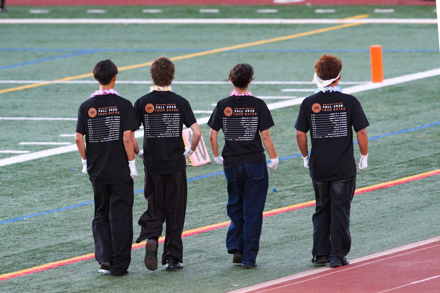Four students in matching black t-shirts walk across a football field during a school event.