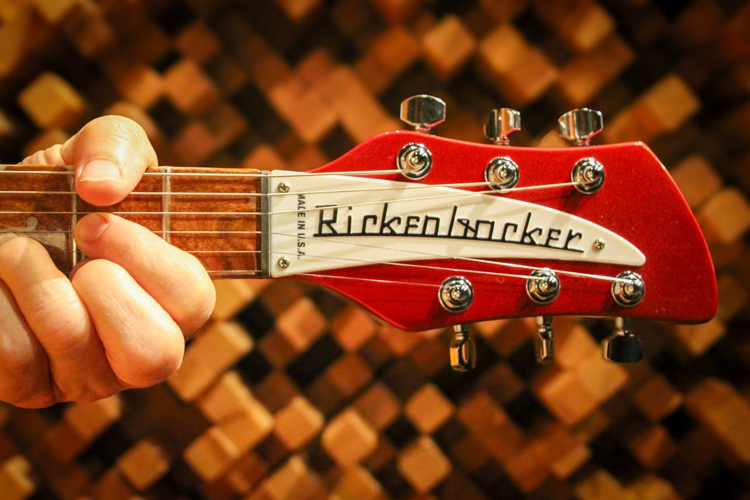 Close-up of a red Rickenbacker electric guitar headstock with tuning pegs, held by a hand against a warm bokeh background.