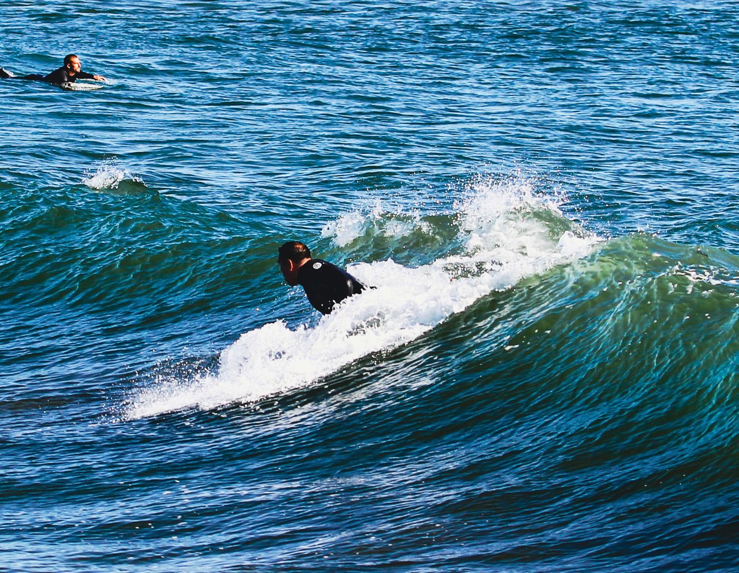 Surfer in black wetsuit skillfully riding a large blue ocean wave.