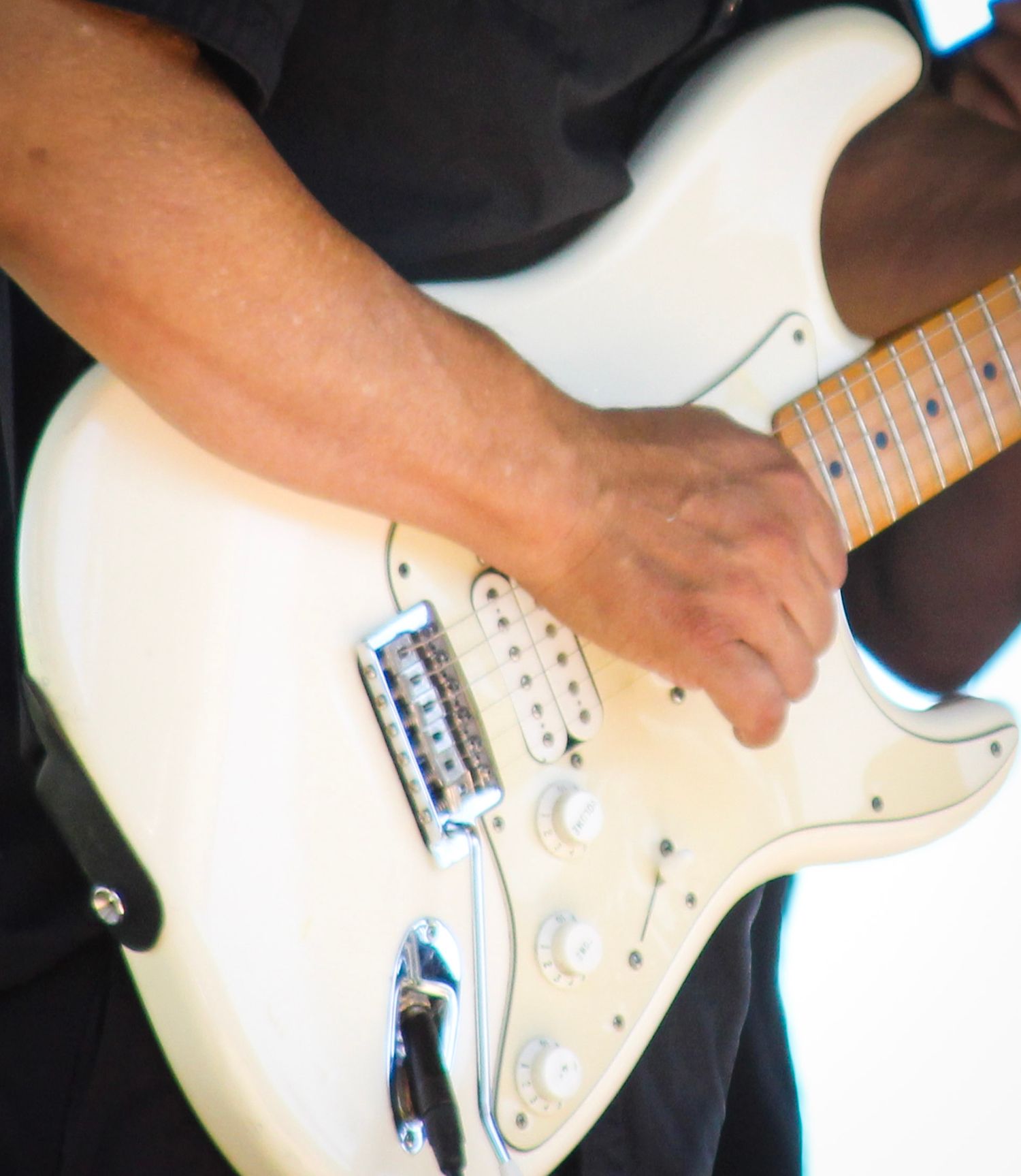 Close-up of a musician playing a white Fender Stratocaster electric guitar with chrome hardware.