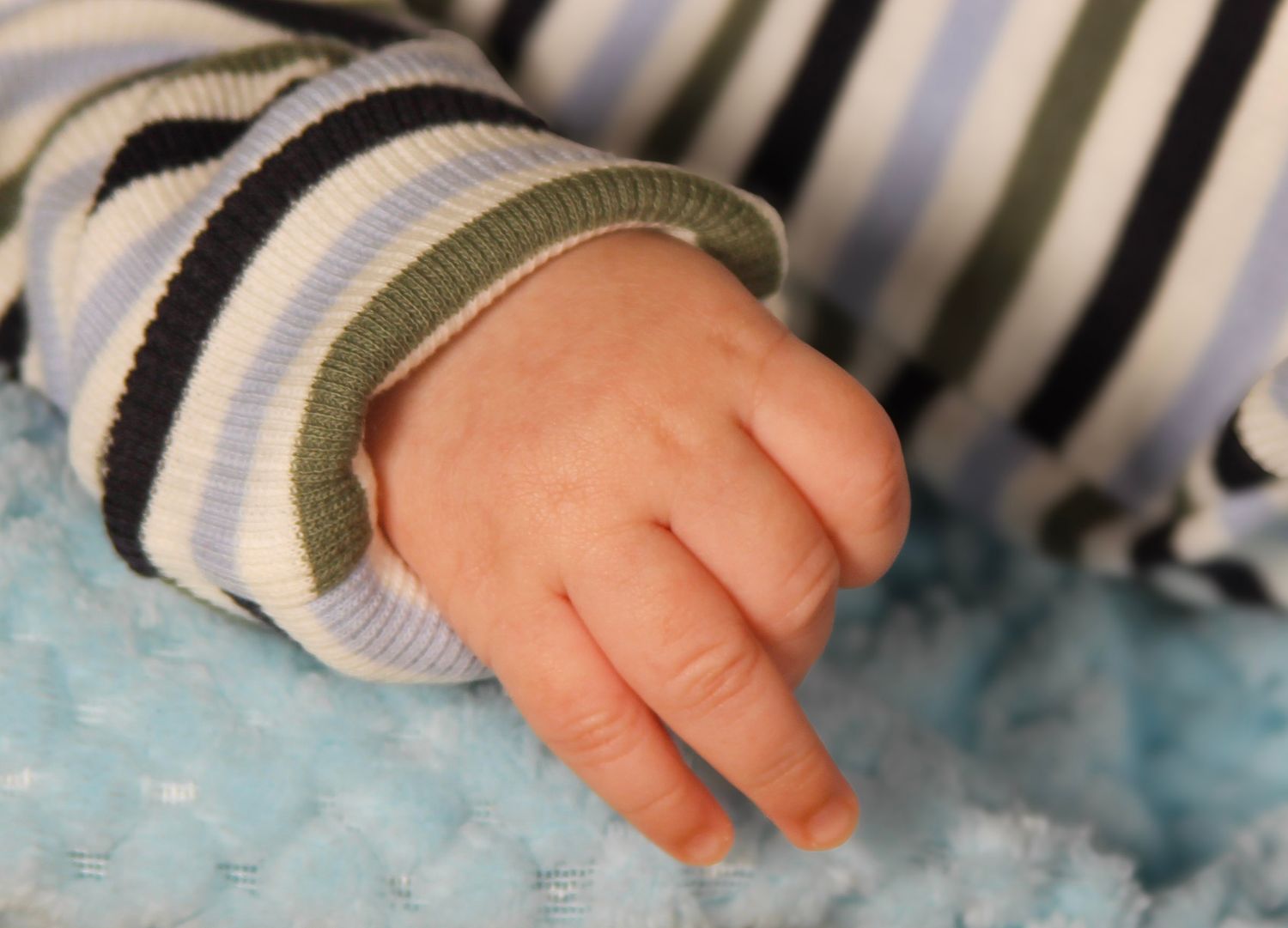 Close-up of a newborn baby's tiny hand resting on a soft blue blanket, wearing a striped onesie.