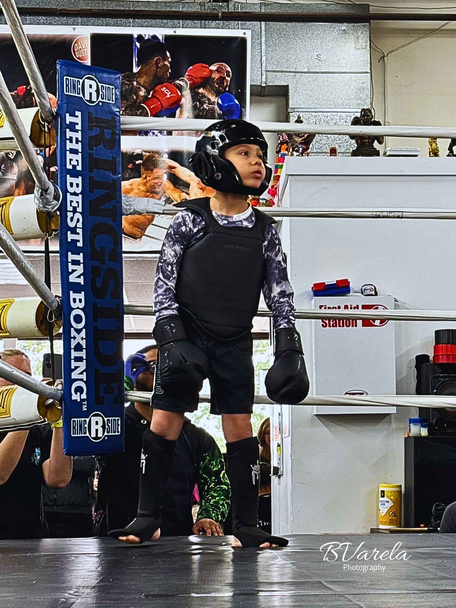 Young boxer in protective gear stands in ring at Ringside boxing gym, wearing helmet, chest guard, and gloves.