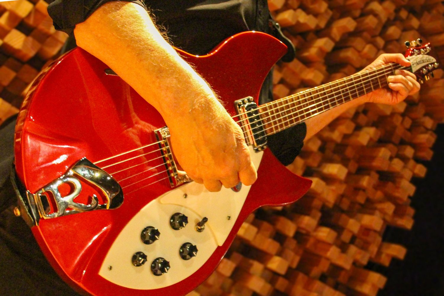 Close-up of a red Rickenbacker electric guitar being played against a warm brick background.