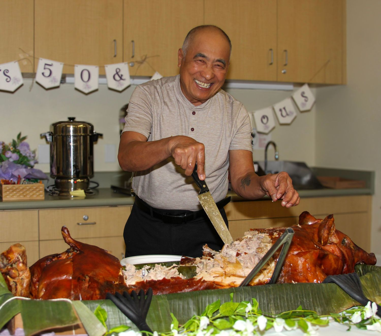 Man smiling while carving roasted pig at a festive celebration with decorative banners in the background.