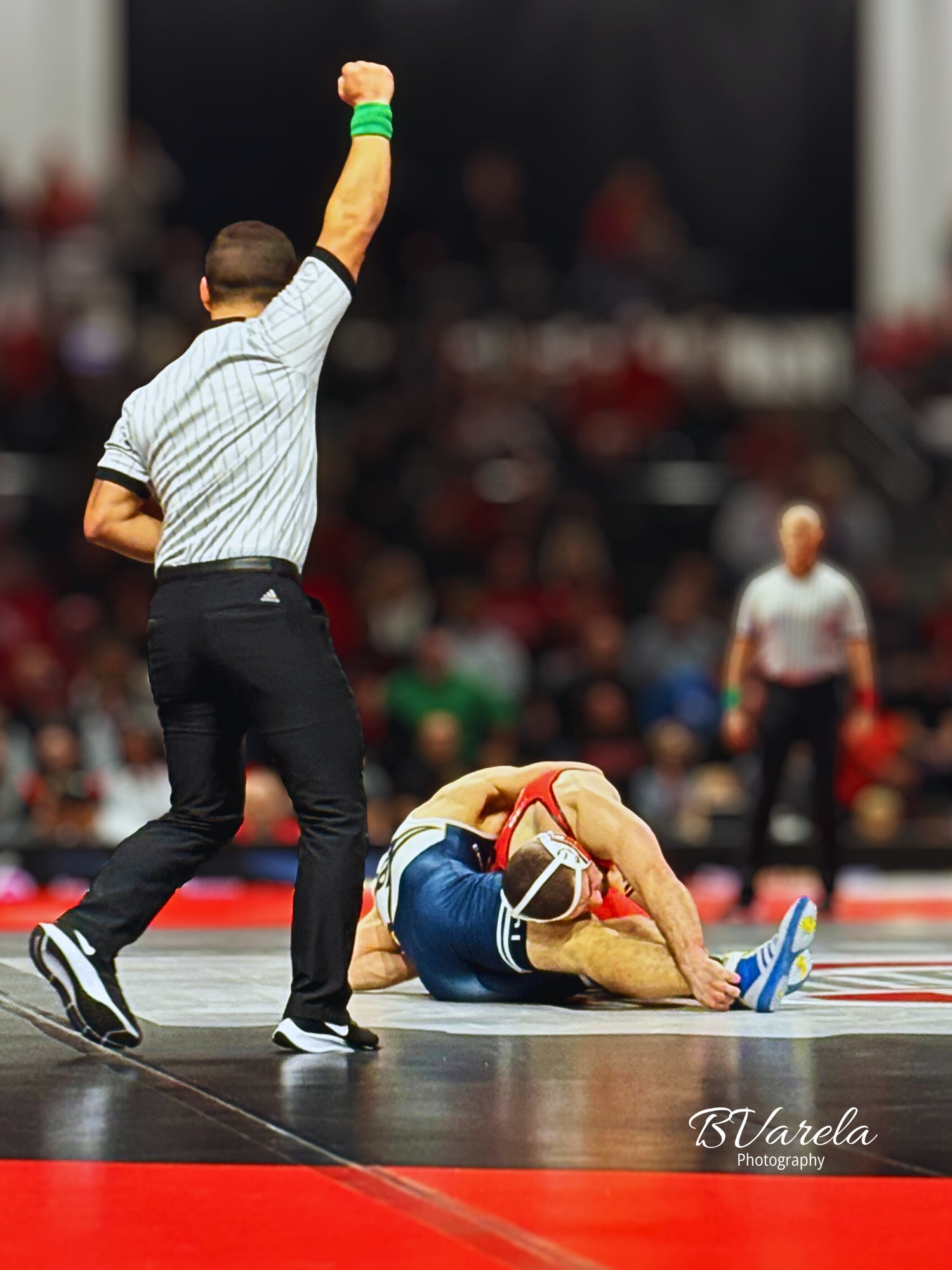 Wrestling referee signals pin as red-uniformed athlete pins opponent on mat. sport photographer