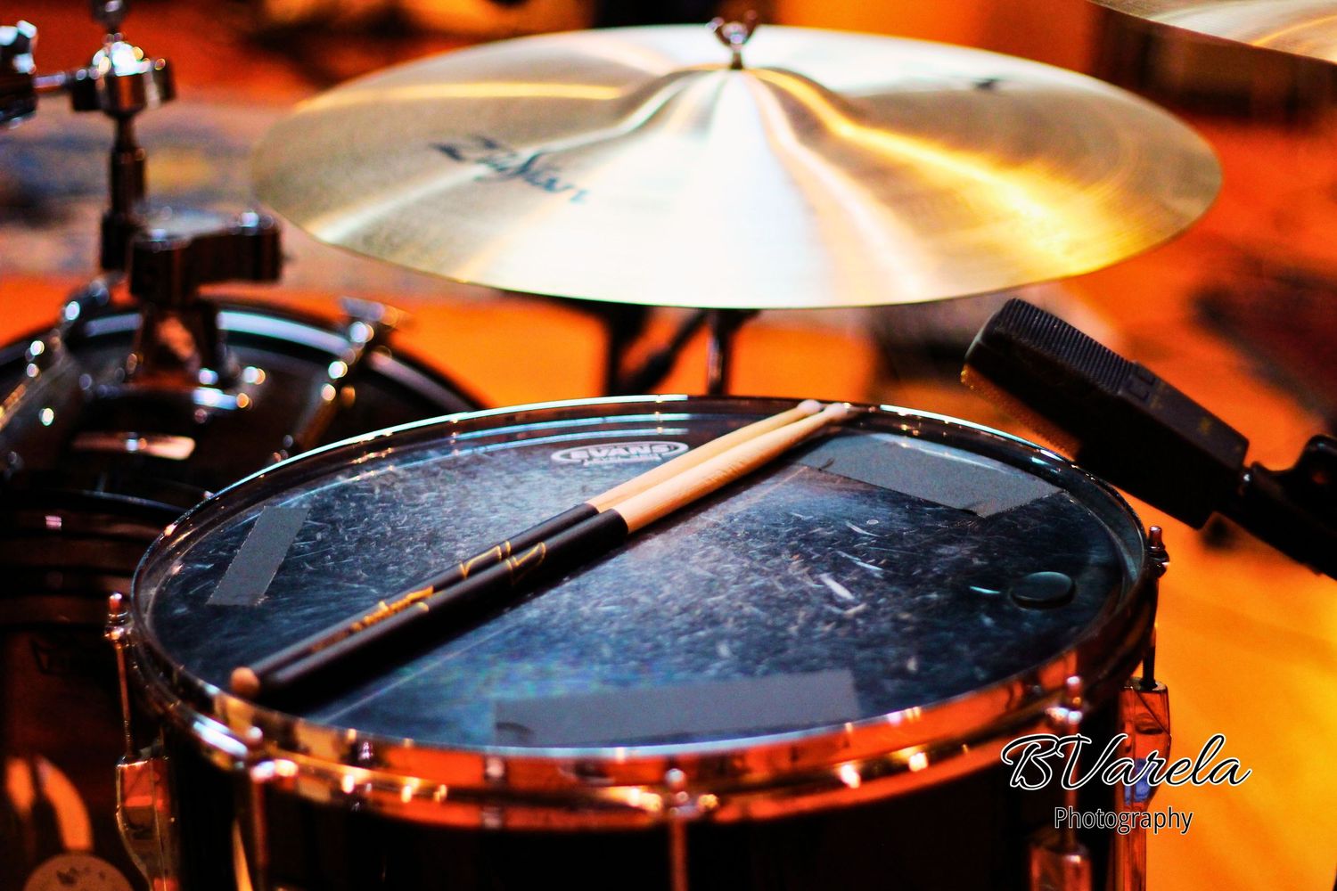 Close-up of a drum kit with drumsticks resting on a snare drum and a shiny cymbal in the background.