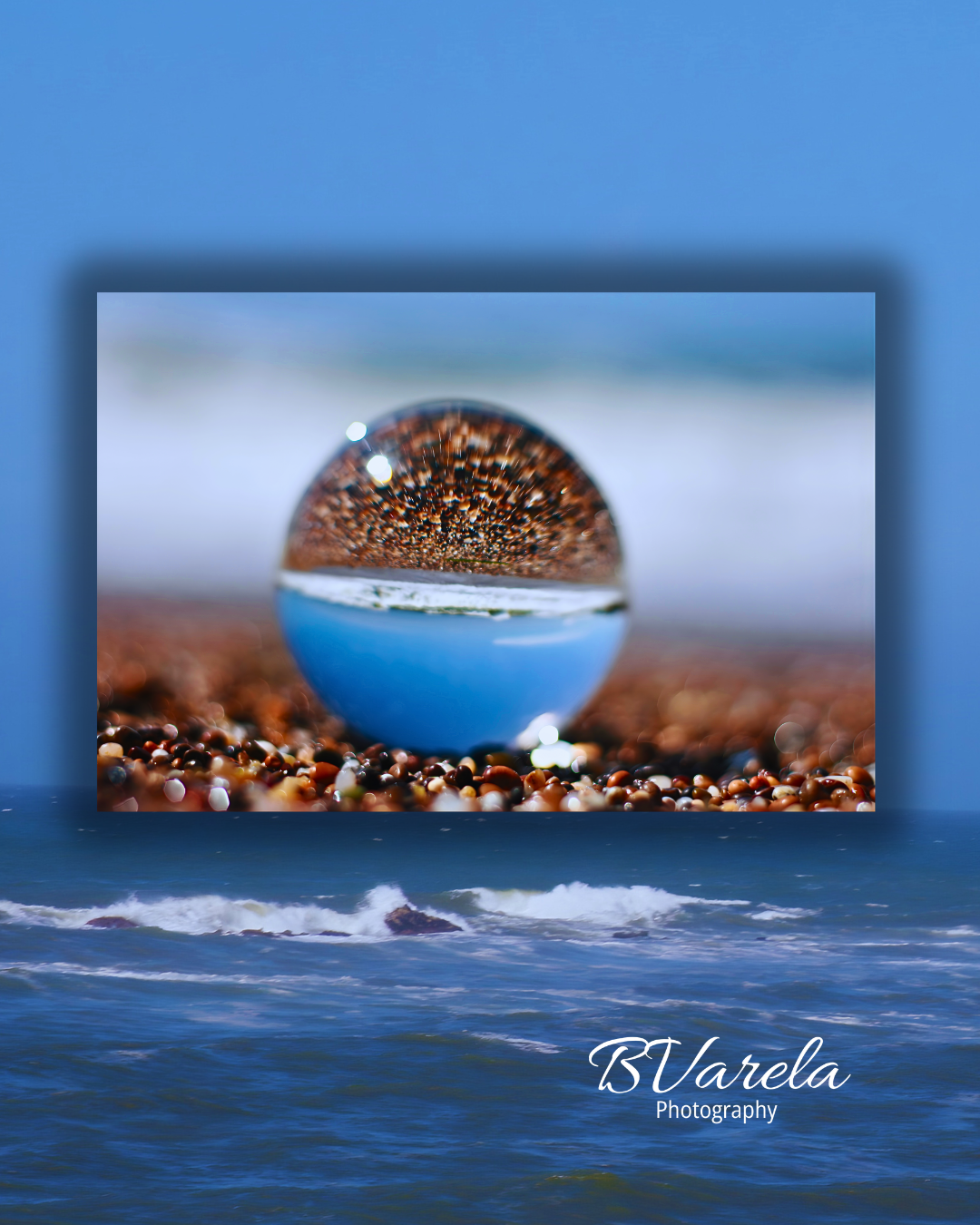 Crystal ball reflecting colorful pebbles on a sandy beach with ocean waves in the background. pesacerdo, photographer
