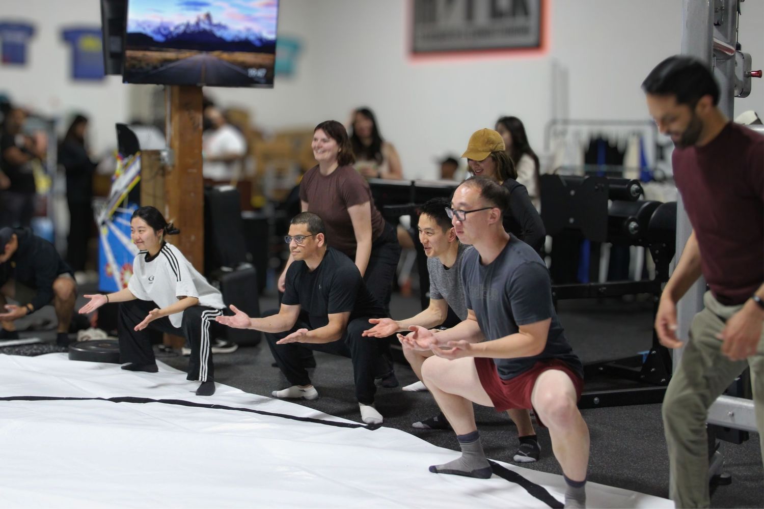 Group of people kneeling in a row at an indoor gym facility during a fitness event or competition.