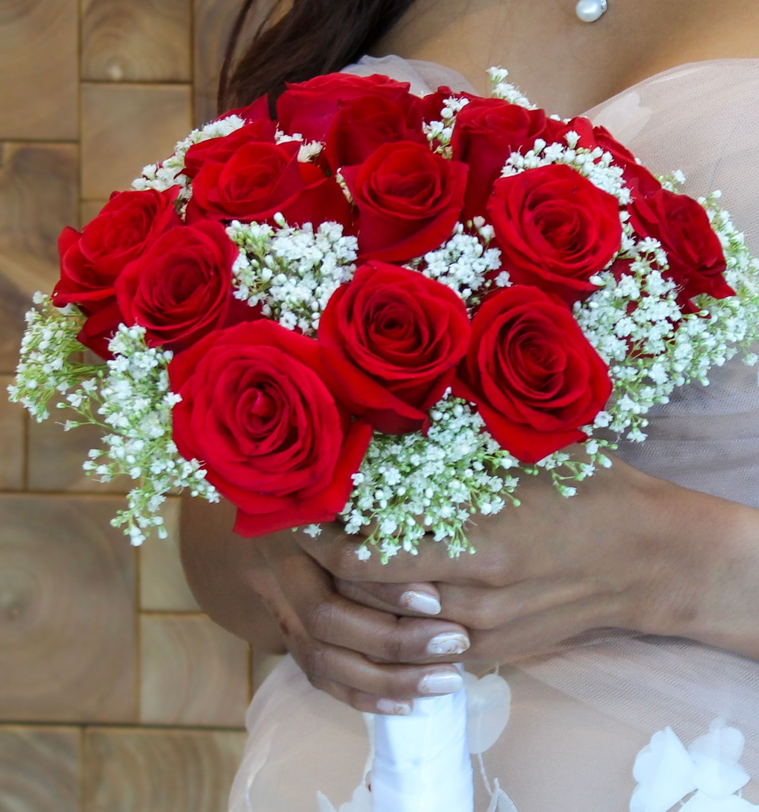 Bride holding a bridal bouquet of red roses and white baby's breath flowers on her wedding day.