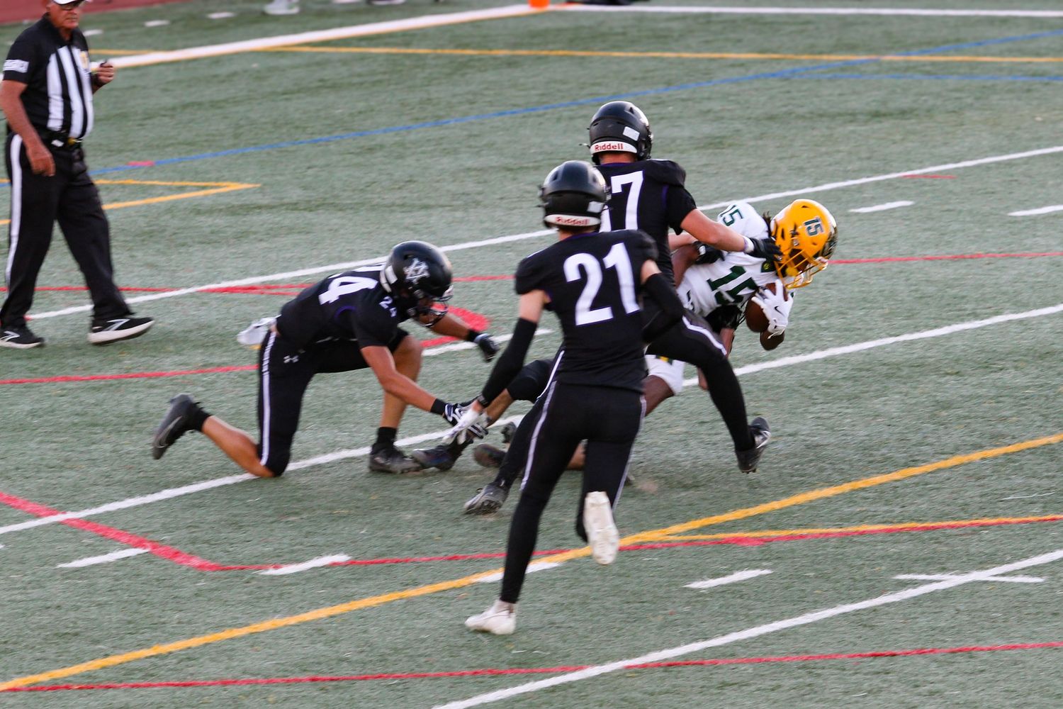 Youth football players in black uniforms tackle an opponent in gold during a competitive game on a marked field.