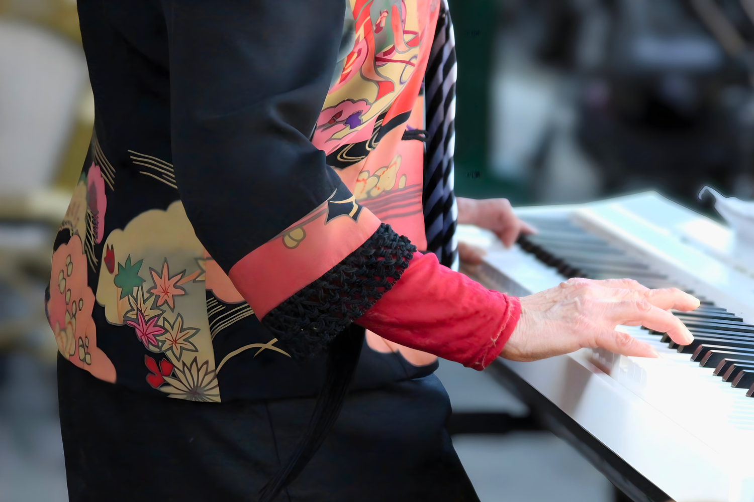 Person in colorful floral kimono playing white electric piano keyboard, close-up of hands on keys.
