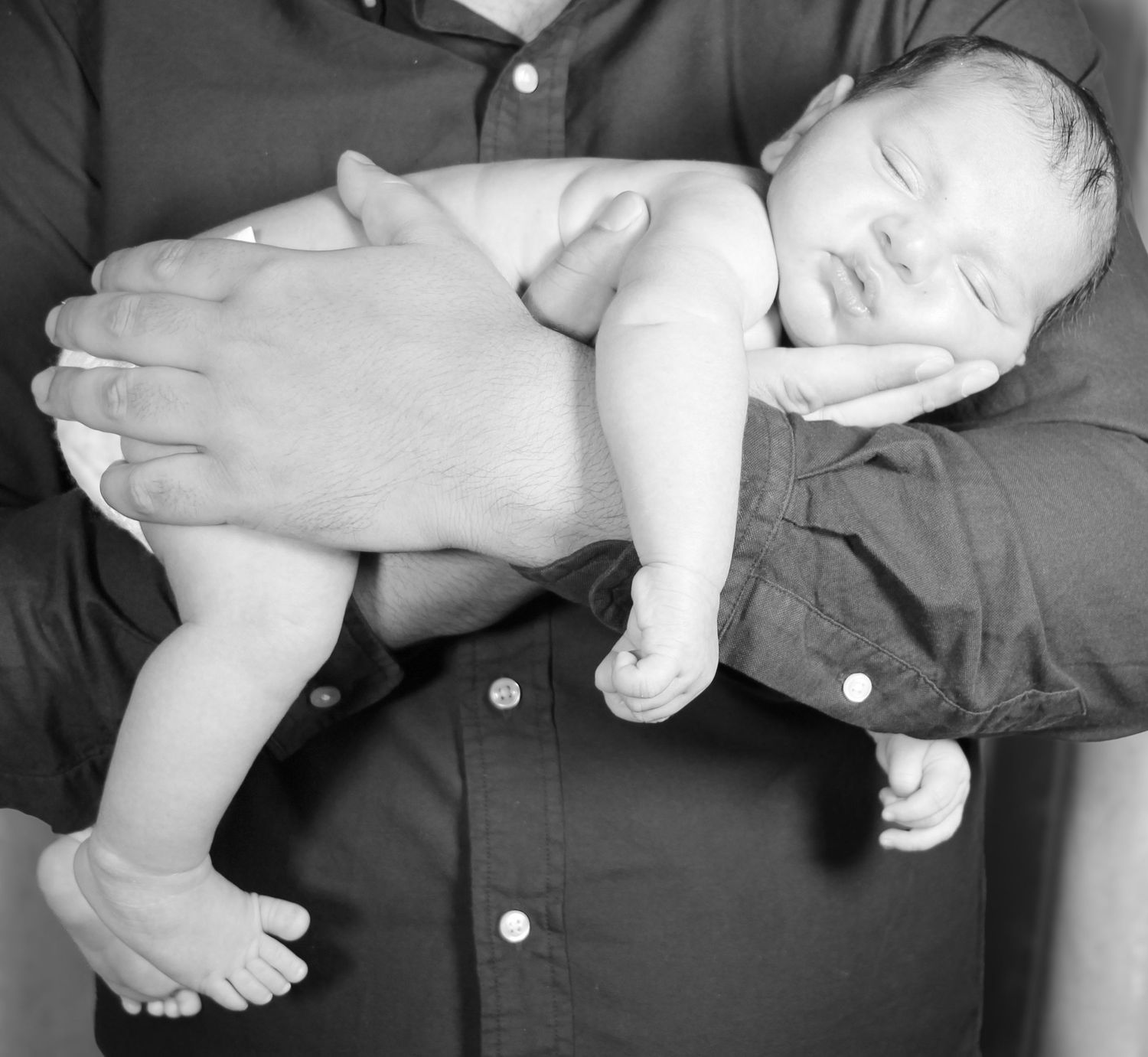 Black and white photo of a newborn baby sleeping peacefully in an adult's hands against their chest.