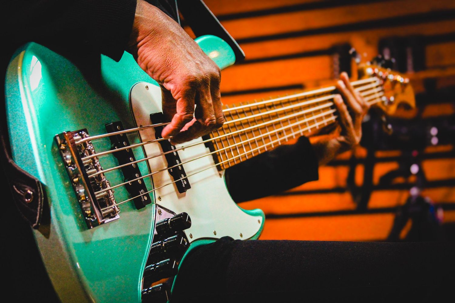Close-up of a musician playing a teal electric bass guitar on a warmly lit stage.