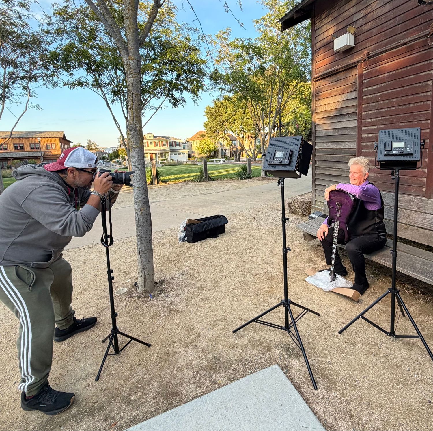 Photographer capturing a portrait of a seated woman outdoors using studio lighting equipment on tripods.