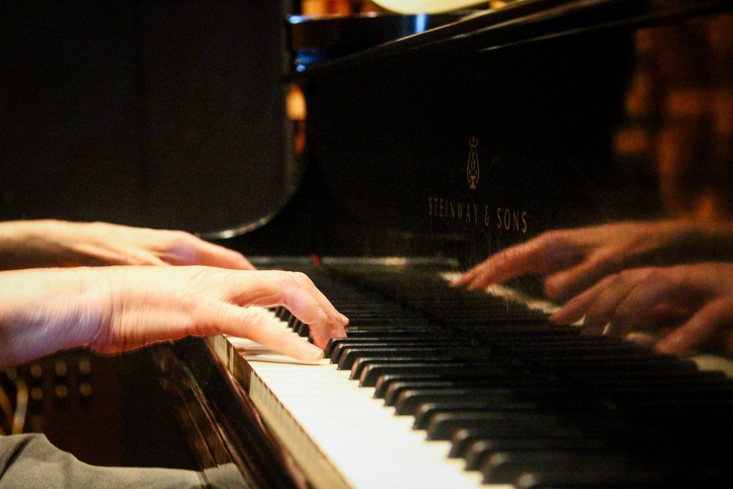 Close-up of hands playing a Steinway & Sons grand piano, fingers gracefully pressing black and white keys.