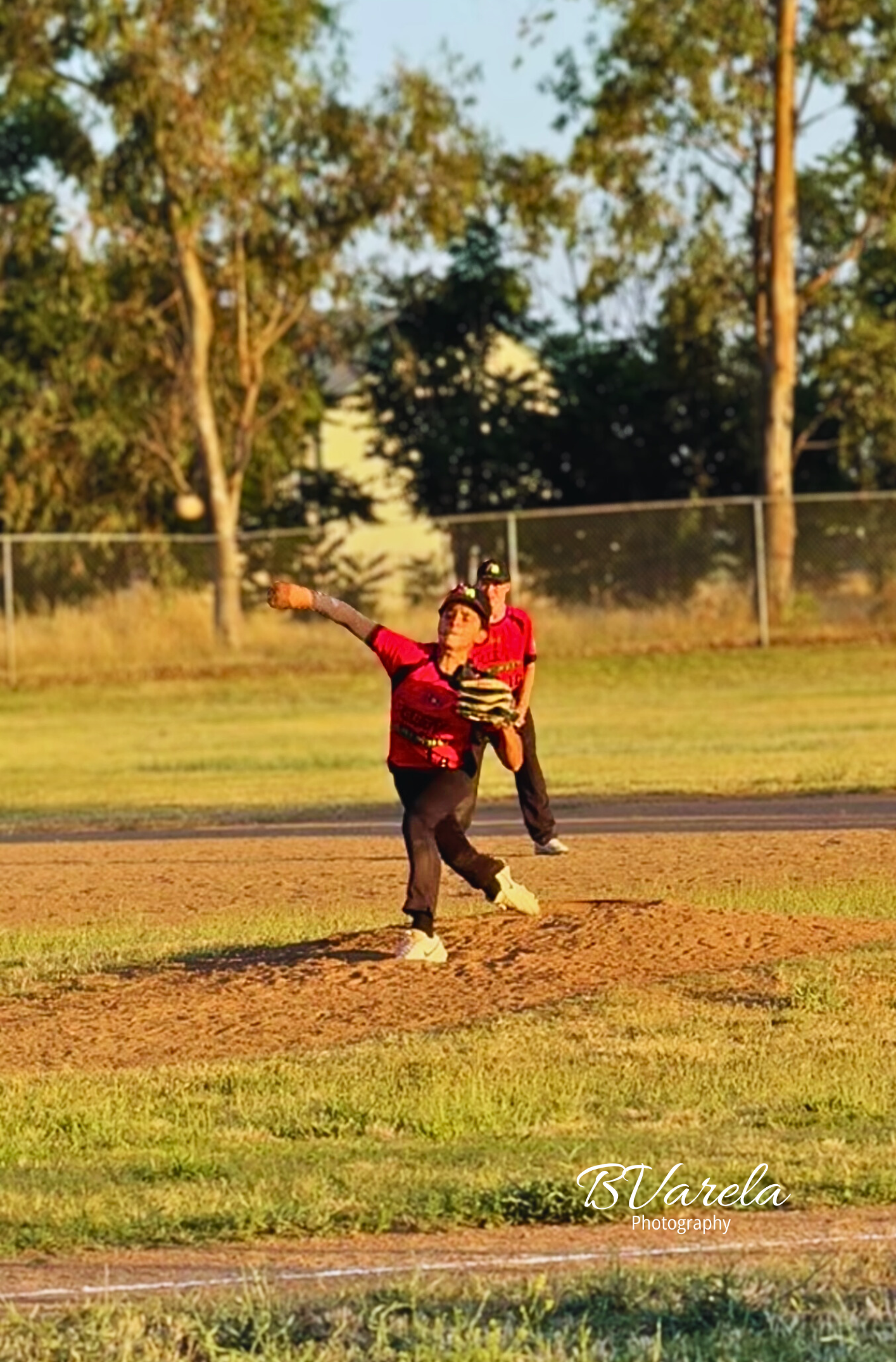 Youth baseball pitcher winds up on mound during evening outdoor game. sport photographer
