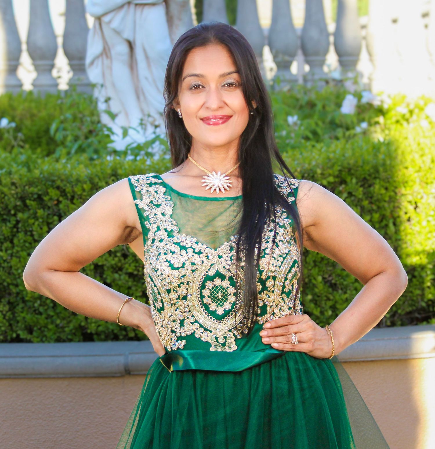 Woman in elegant green and gold embroidered lehenga posing outdoors with hands on hips, smiling confidently.
