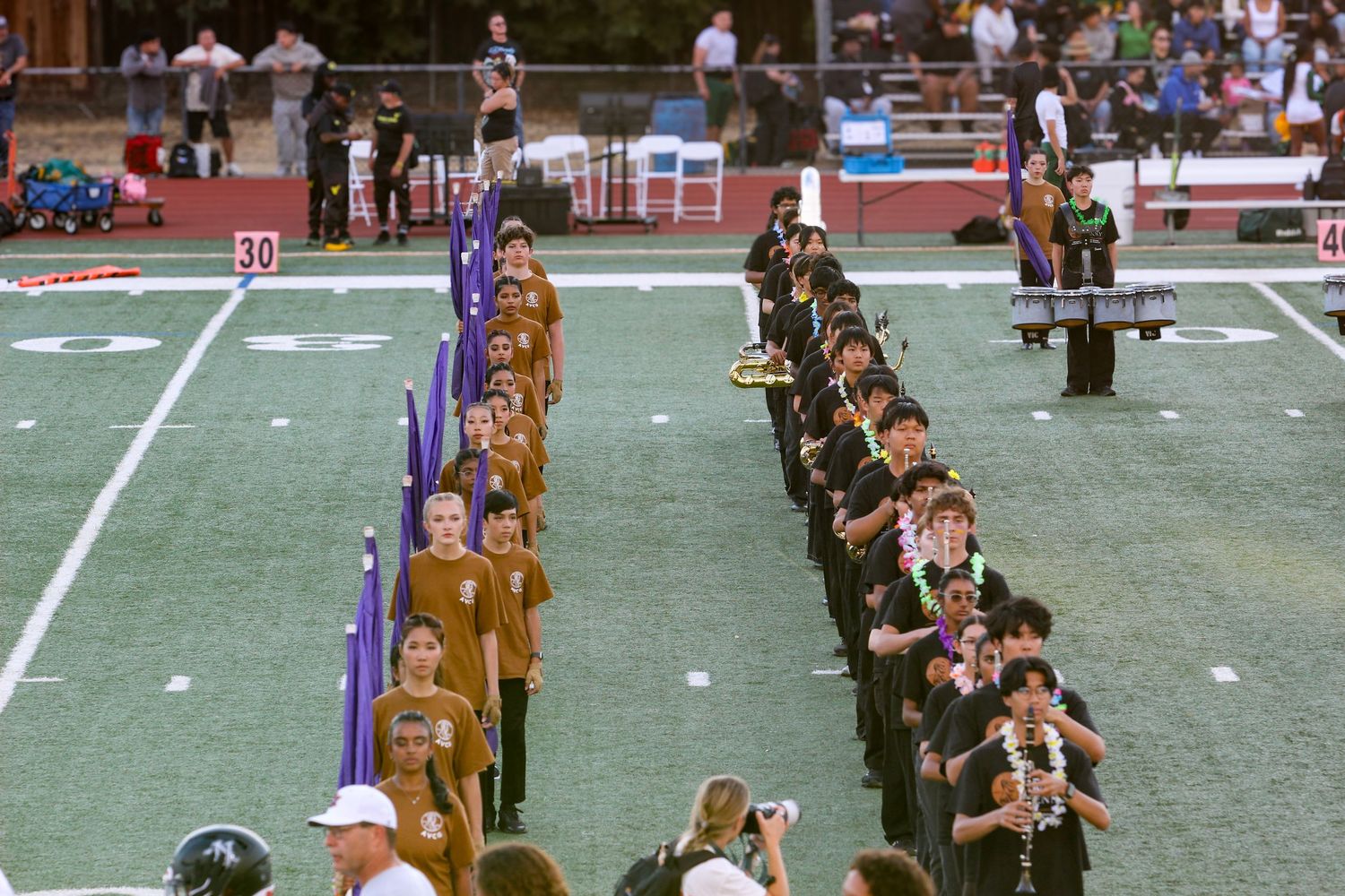 Marching band students perform in formation on a football field during a halftime show at a stadium.